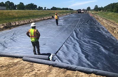 Photo: Crews place geotextile fabric to asphalt paving to measure its effect on moisture wicking at MnROAD.